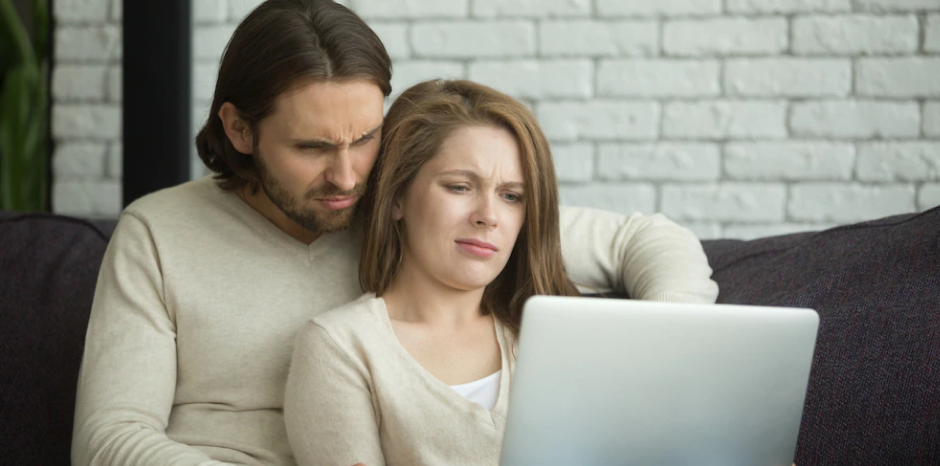 Concerned-looking couple browses the internet on their laptop