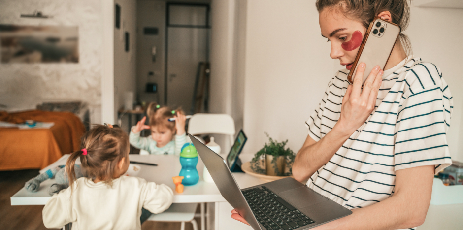 Women property practitioner uses her laptop and phone as children play in background